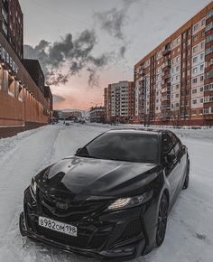 a black car parked in the middle of a snow covered street next to tall buildings