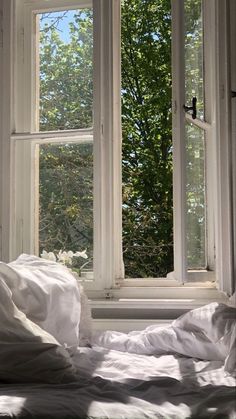 an open window with white sheets and trees in the background