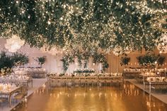 an indoor wedding reception setup with tables and chandeliers hanging from the ceiling, surrounded by greenery