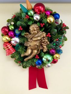 a christmas wreath hanging on the wall next to a red ribbon with an angel holding a baby