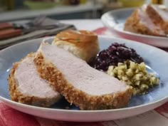 two white plates with meat, stuffing and cranberry sauce on them sitting on a table