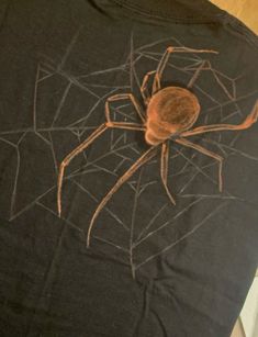 a black t - shirt with a spider on it's chest and brown web