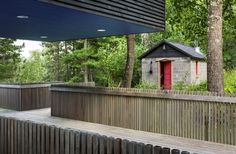 a wooden bench sitting under a red door next to a forest filled with green trees