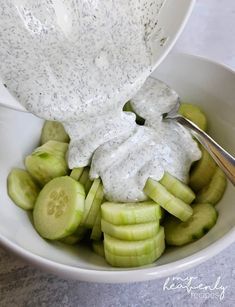 a bowl filled with cucumbers and dressing being drizzled