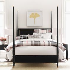 a black and white bed with plaid comforter, pillows and blankets on the headboard