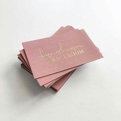 four folded pink cards with gold foil lettering on the front and back, sitting next to each other