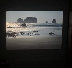 an ocean view through a window with rocks in the water and one rock outcropping