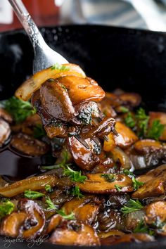 a spoon full of cooked mushrooms with parsley on top in a black skillet