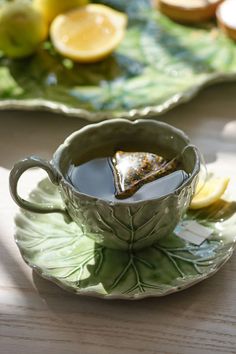 a cup of tea with lemon slices and leaves on the saucer next to it