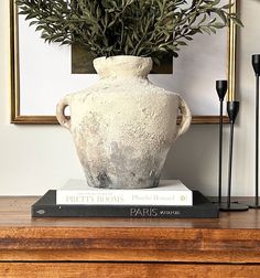 a white vase sitting on top of a table next to two black candles and a book