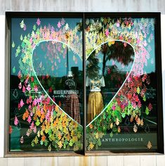 a store window decorated with colorful flowers and leaves in the shape of a large heart