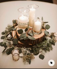 candles and greenery are arranged on a wood slice