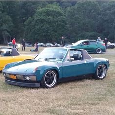 several cars parked in a field with trees in the background and people looking at them