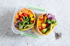 two burritos filled with veggies sit in a plastic container