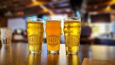 three beer glasses sitting on top of a wooden table