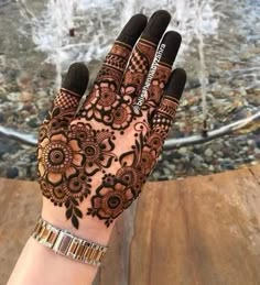 a woman's hand with henna on it and water fountain in the background