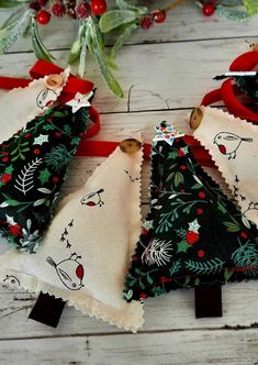 three pieces of cloth with christmas trees on them sitting next to holly wreaths and red ribbon