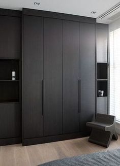 a bedroom with black cabinets and a gray chair next to it on a wooden floor