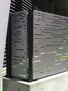 two large metal boxes sitting on top of a cement block next to a building with black shutters