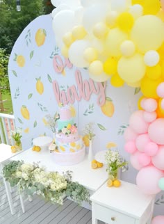 a table topped with a cake next to a bunch of yellow and pink balloons in the shape of pineapples