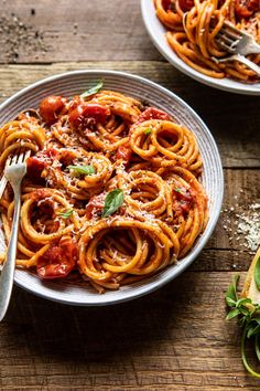 two plates of spaghetti with tomato sauce and parmesan cheese on the side next to a fork