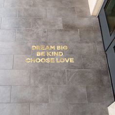 the words dream big be kind choose love are written in gold on a gray tile floor