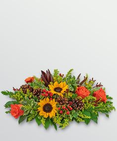 an arrangement of sunflowers, roses and greenery with pine cones in the center