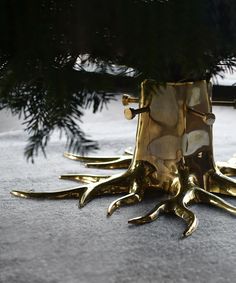 a gold vase sitting on top of a floor next to a pine tree with it's roots sticking out