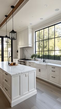 a large kitchen with white cabinets and marble counter tops, along with black framed windows