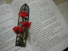 an open book with some red flowers on top of it and a black metal frame