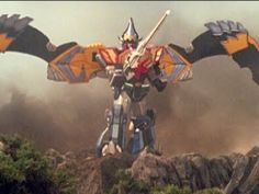 a giant robot standing on top of a rocky hill next to grass and rocks in the background