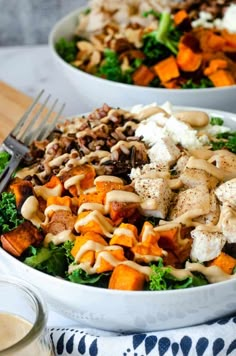 two white bowls filled with salad and dressing on top of a wooden table next to a fork