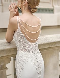 a woman in a white wedding dress leaning on a ledge with her hands clasped to her chest