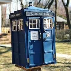 a blue phone booth sitting on top of a wooden post in front of a house