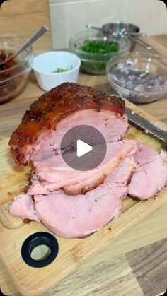 a wooden cutting board topped with sliced meat on top of a table next to bowls and utensils