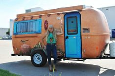 a woman standing in front of an orange trailer with blue doors and windows, on the sidewalk