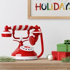 an old fashioned red phone sitting on top of a wooden table next to christmas presents