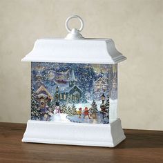 a christmas scene is displayed in a glass container on a wooden table with an ornament hanging from the top