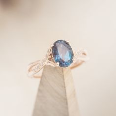 an oval blue sapphire and diamond ring on top of a wooden stand in front of a white background