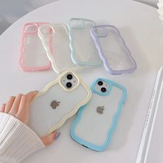 four iphone cases sitting on top of a white table next to a person's hand