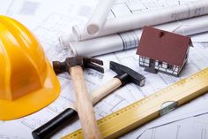 some construction tools are laying on top of blueprints and pencils with a house model in the background