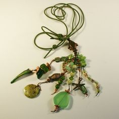 a necklace with green beads and charms on a white surface, next to a brown cord