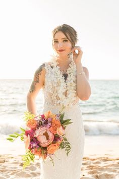 a woman in a wedding dress on the beach holding a bouquet and talking on her cell phone