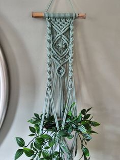 a macrame hanging from a wall next to a potted plant with green leaves