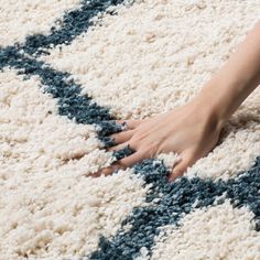 a person's hand on a rug with blue and white colors