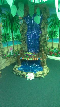 a fake waterfall in the middle of a room with palm trees and decorations around it