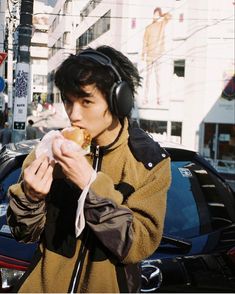 a young man wearing headphones and eating a doughnut on the street in front of a car