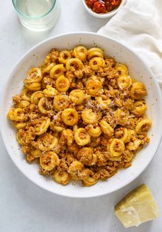 a white bowl filled with pasta and sauce next to a glass of water, lemon wedges and salt