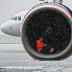 a man in an orange vest is sitting on the nose of a jet airliner