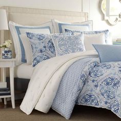 a bed with blue and white comforters in a bedroom next to a mirror on the wall